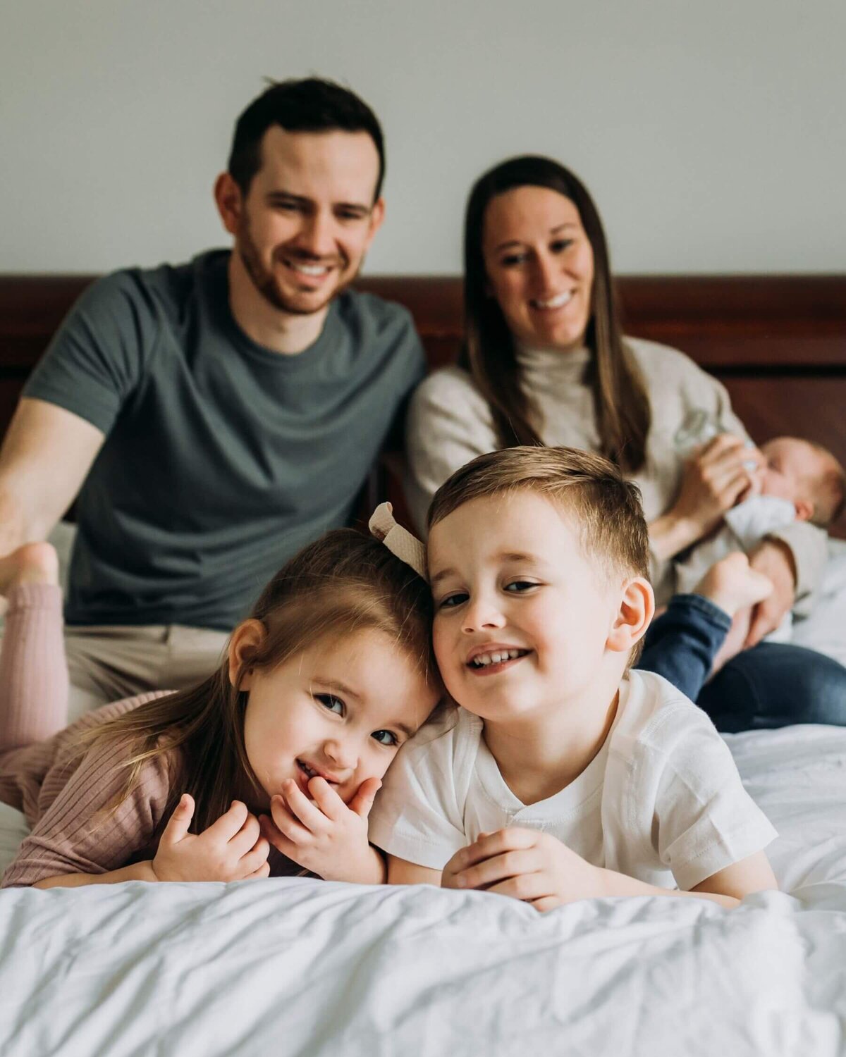 A Pittsburgh family photographer captures a family sitting on a bed and smiling at the camera.