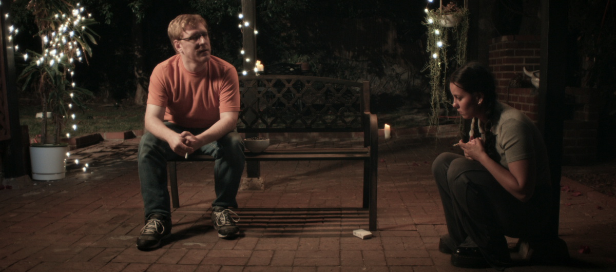 Man sitting on bench in yard talking to girlfriend sitting on the ground