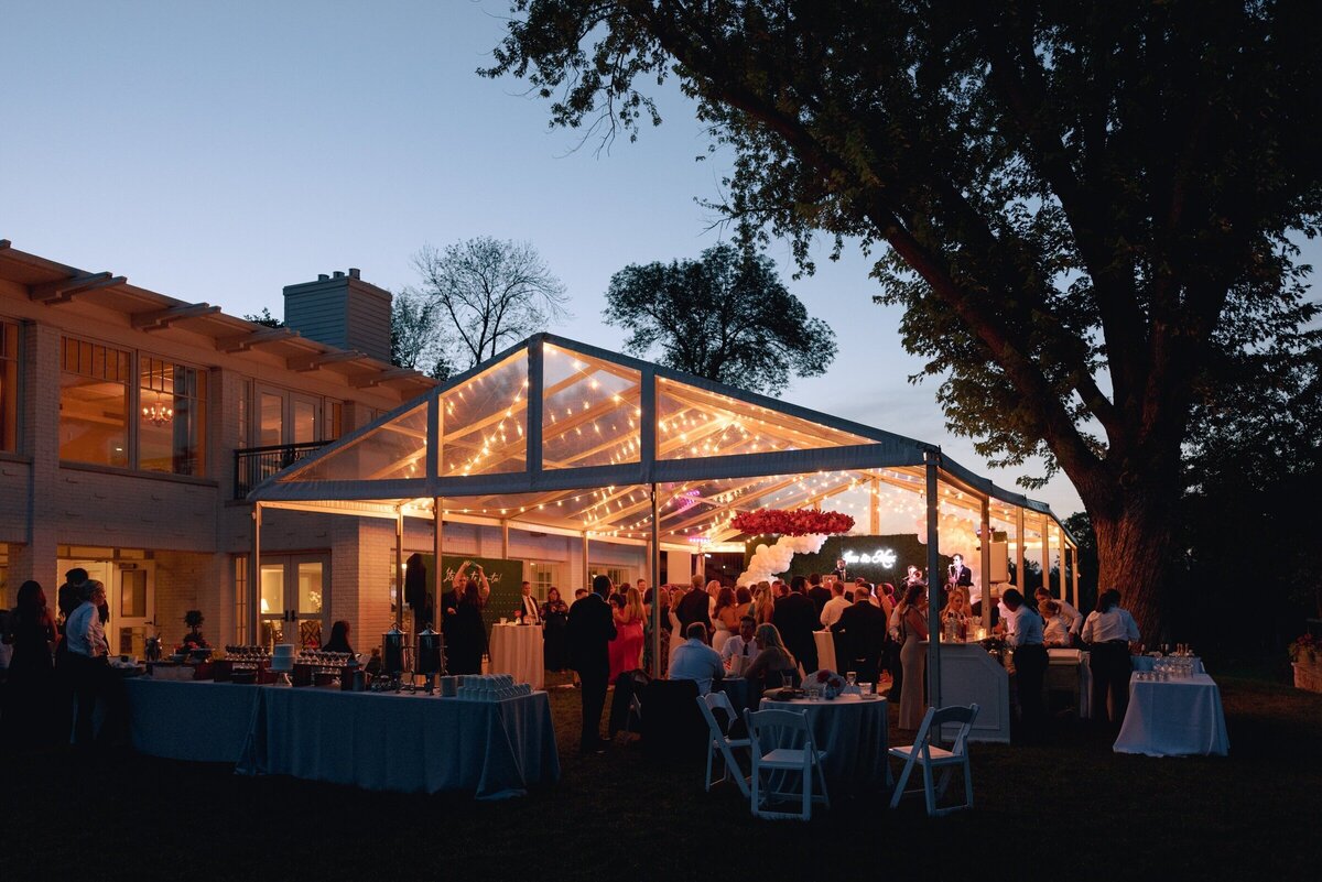 dusk setting wedding reception with guests warmly lit under white tent photographed by minnesota photographer tom thornton 