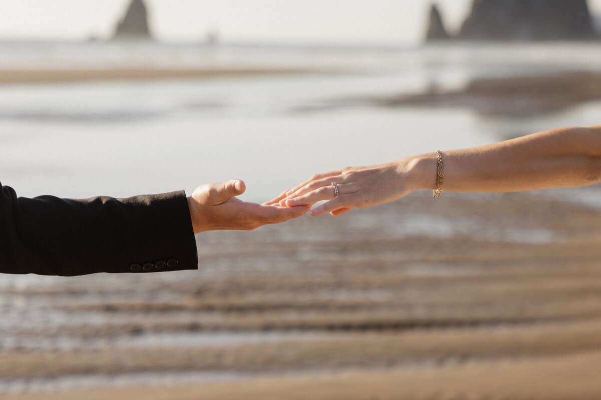 Bride and groom reach for each other's hands during their intimate Cannon Beach ceremony.