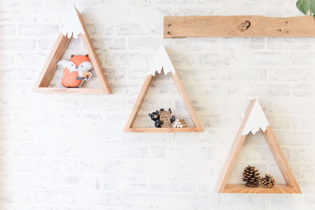 Baby shower wall decorations featuring mountain peak shelves adorned with woodland elements such as bears, pinecones, and other forest-themed accents for a baby boy’s shower.