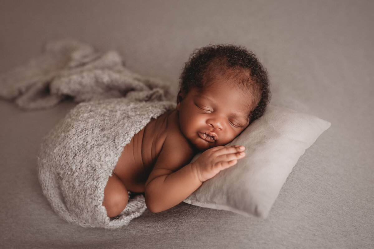 Newborn baby boy asleep on tiny white pillow and posed on gray soft fabric