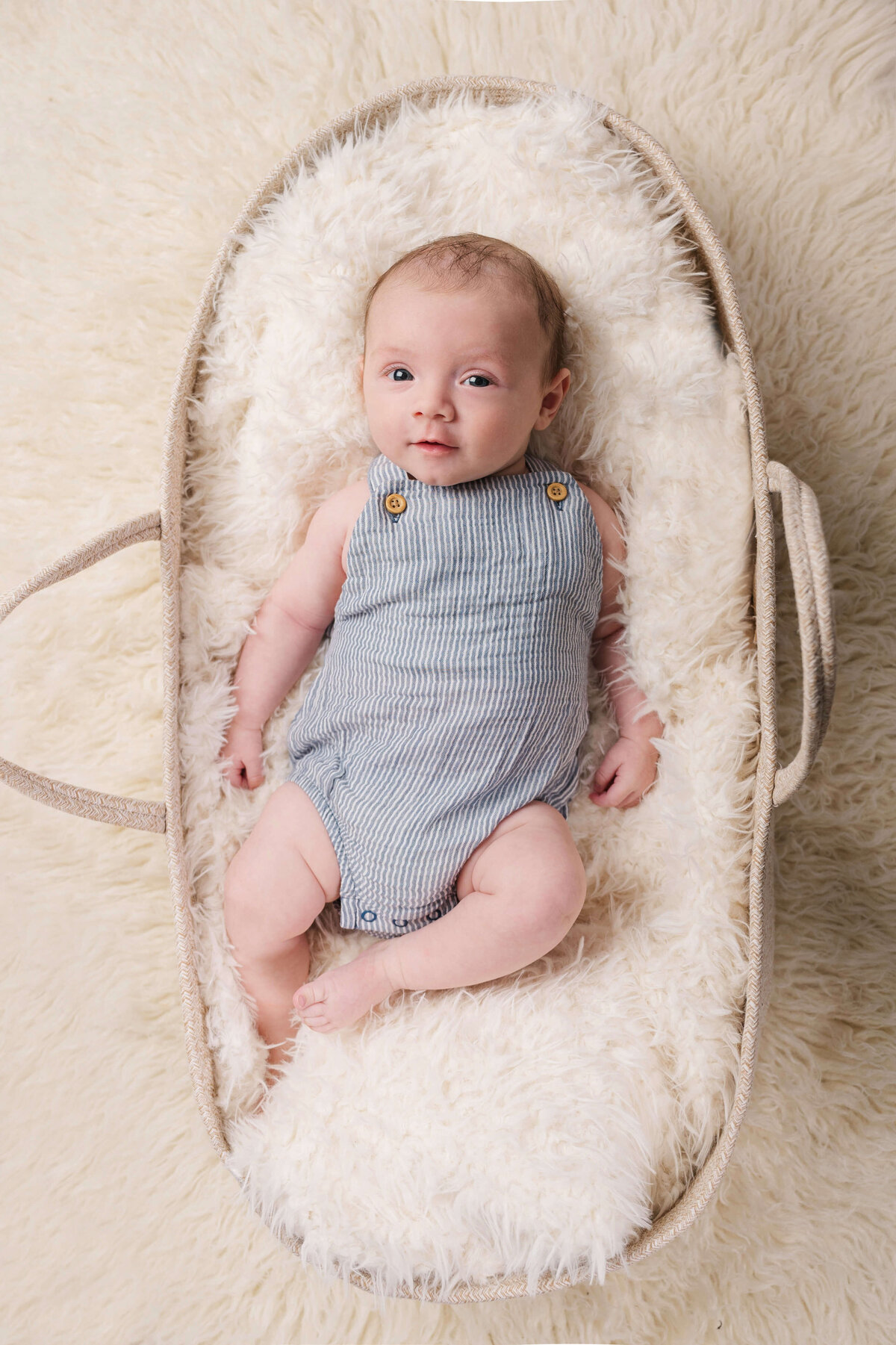 A Raleigh newborn wearing overalls and laying in a Moses basket.