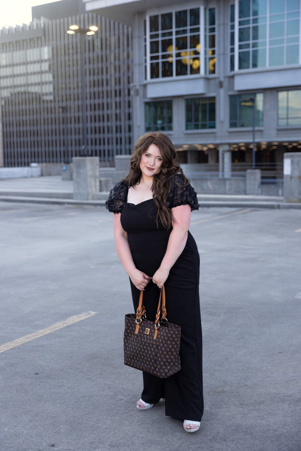 Cute high school senior wearing a black jump suit with a fancy purse.