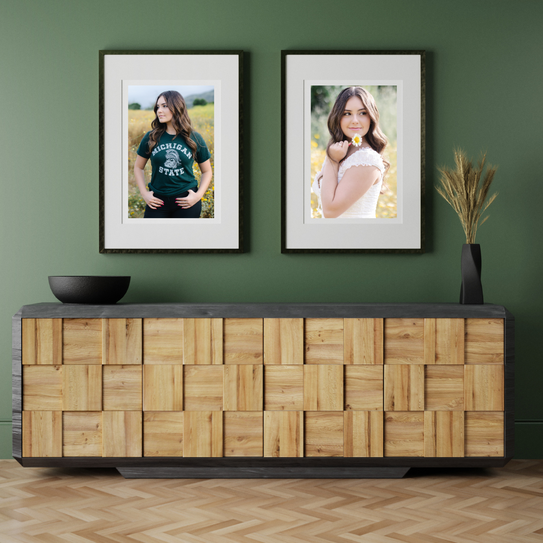 A green wall with a wooden cabinet beneath it in a modern entryway with two black framed photographs of a young woman with long, brown hair, one picture with her holding a flower in a white dress in a field, the other with her wearing a green t-shirt that reads "Michigan State" in the same field of flowers.