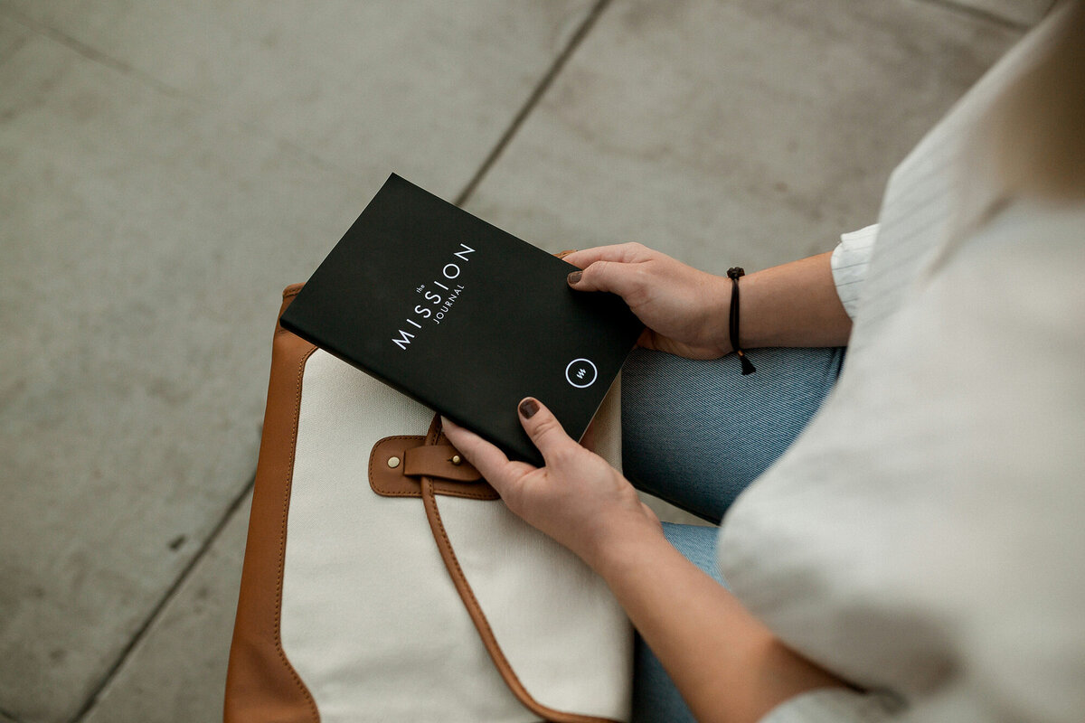 Close-up of a sitting woman holding a black journal with the words "Mission Journal," symbolizing financial clarity and strategic business growth. Ataraxis Financial provides accurate, educational bookkeeping services to help aspiring 7-figure business owners simplify finances, gain confidence, and thrive.