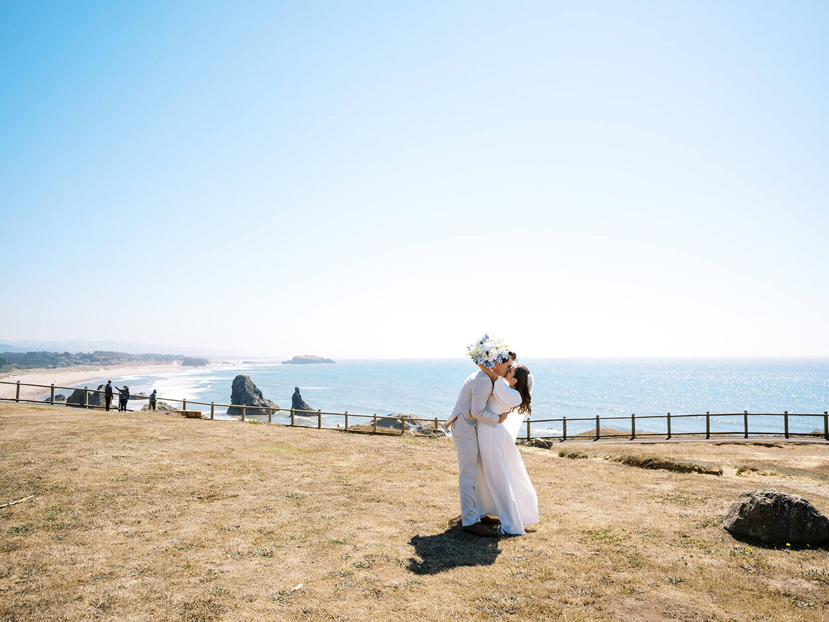 Bride and groom embrace on a cliff overlooking the ocean.