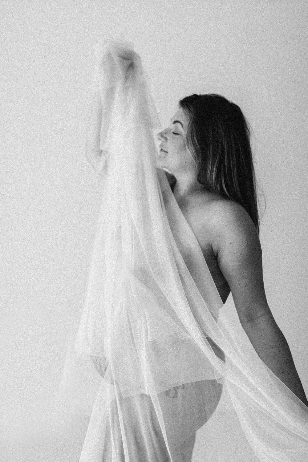 Woman holds fabric across her naked body and dances