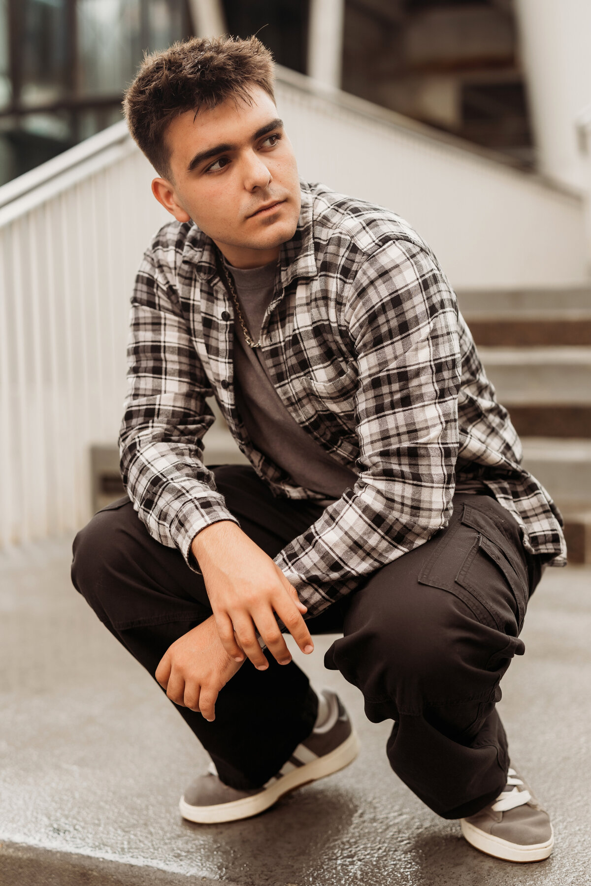 high school senior boy squats on the landing of concrete steps downtown Denver for his senior photos