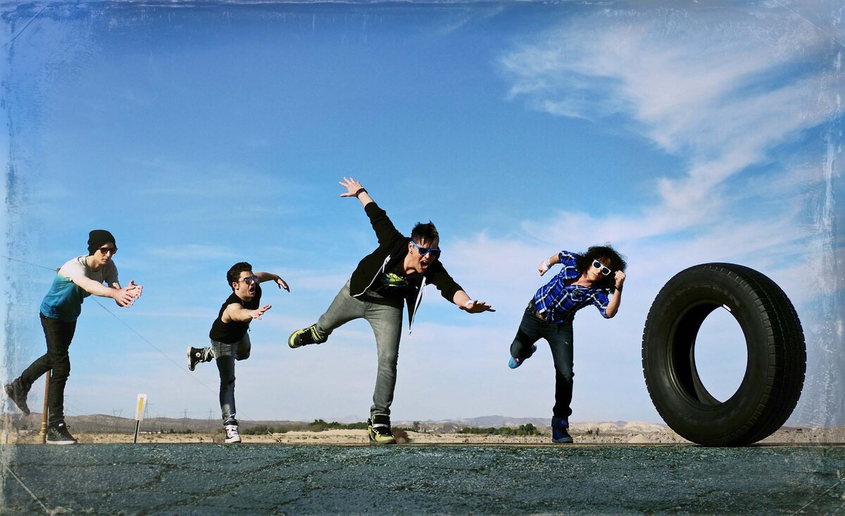Musical band photo Faber Drive chasing rolling tire down street under blue sky