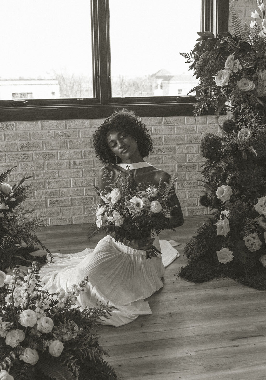 A person in a wedding dress sitting on the floor holding a bouquet of flowers.