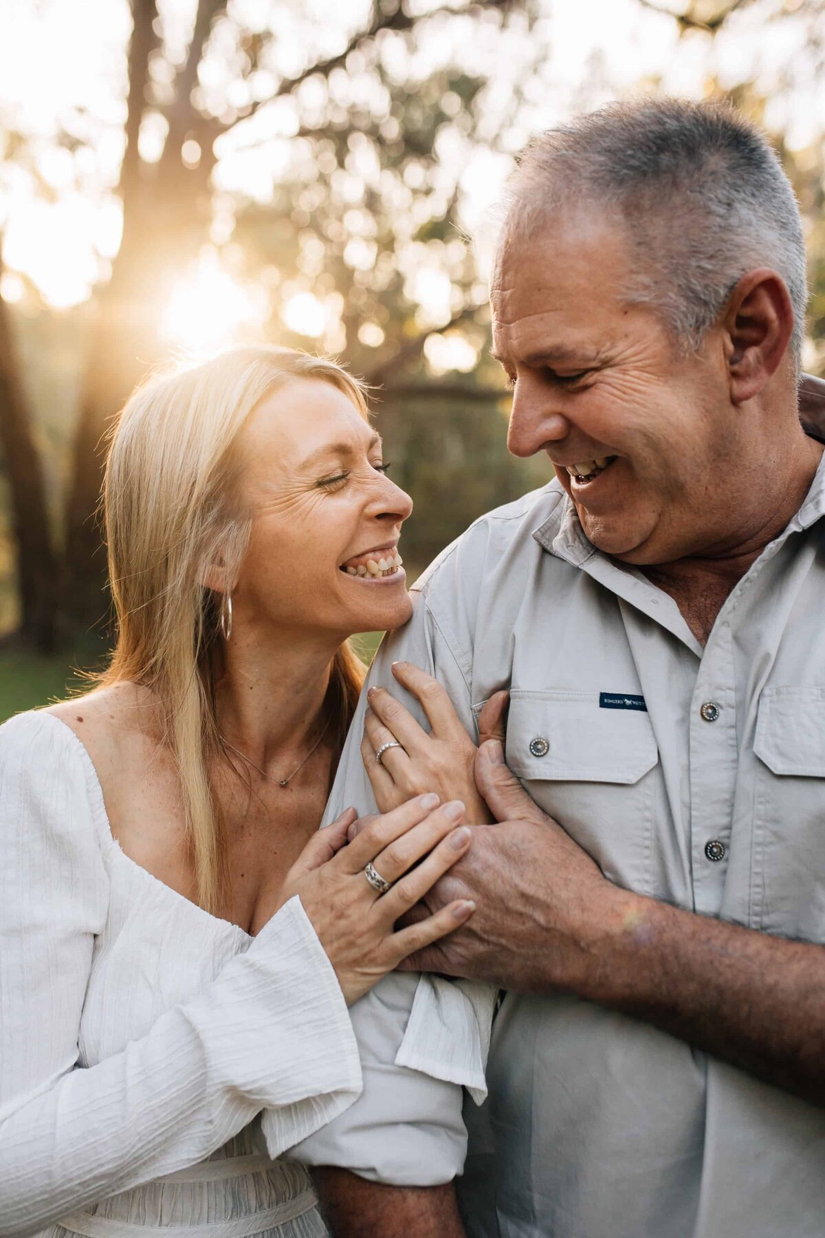 Mature age couple, grinning at each other, her hands wrapped around his arm. Mature couple photoshoot Melbourne, And So I Don't Forget Photography