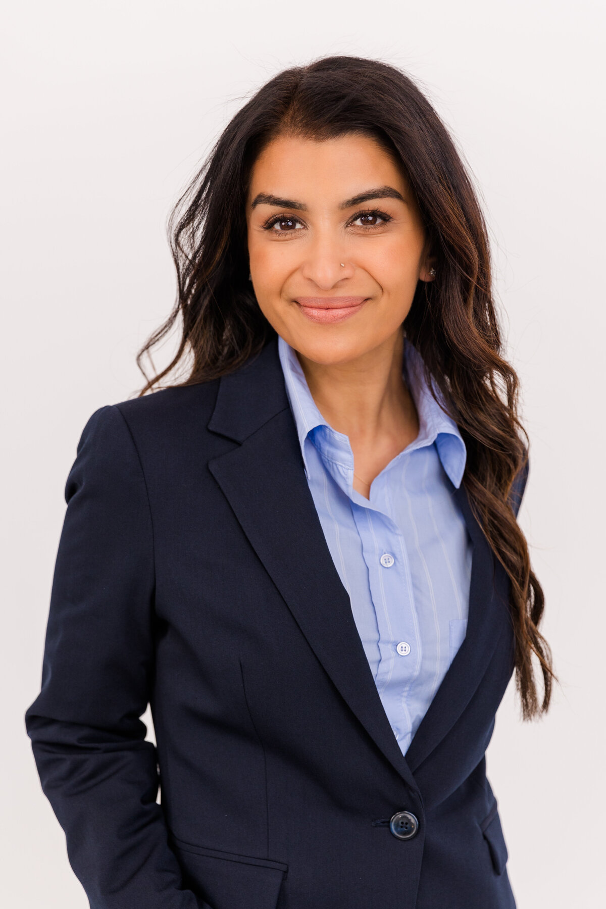 Woman with long dark hair wearing corporate outfits blue button down shirt and navy blue jacket in front of a white backdrop during headshot in Atlanta Buckhead studio with Laure Photography