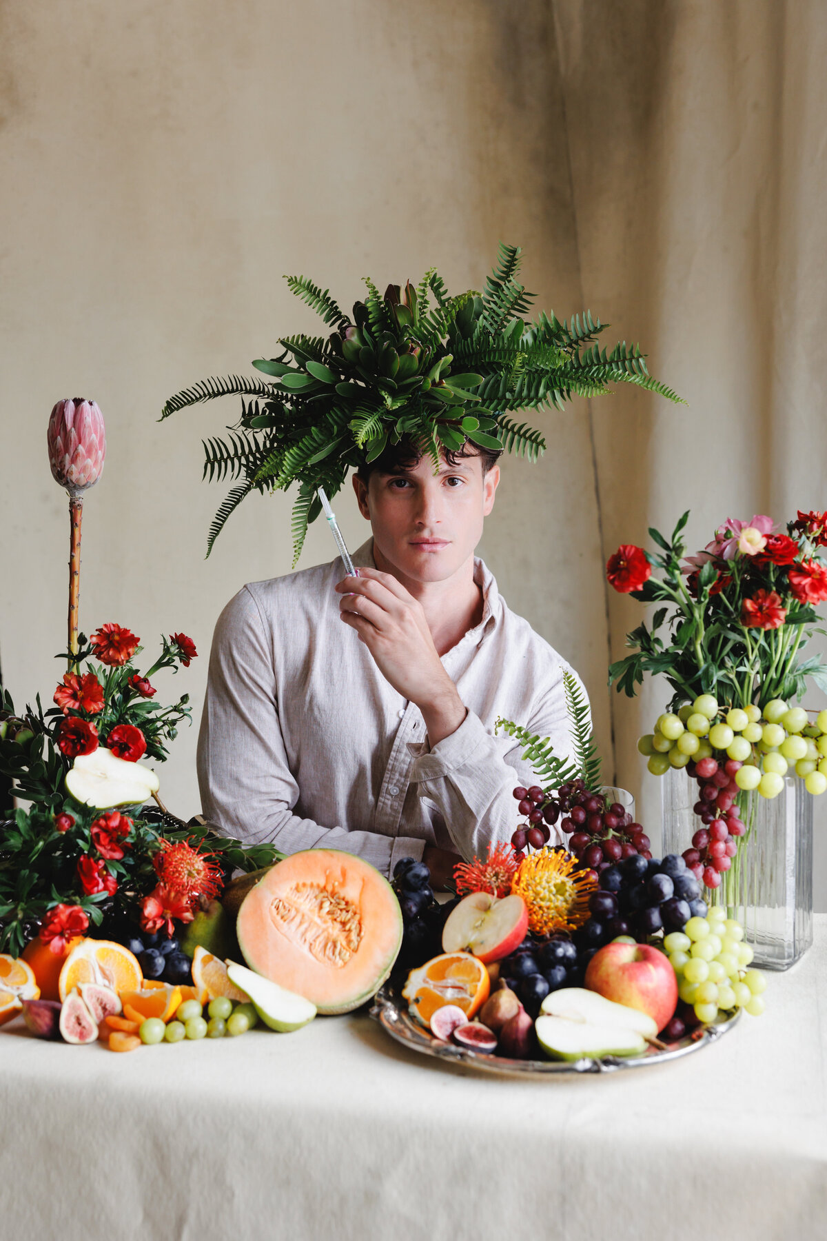 Editorial style portrait of a man surrounded by fruits with a fern headpiece