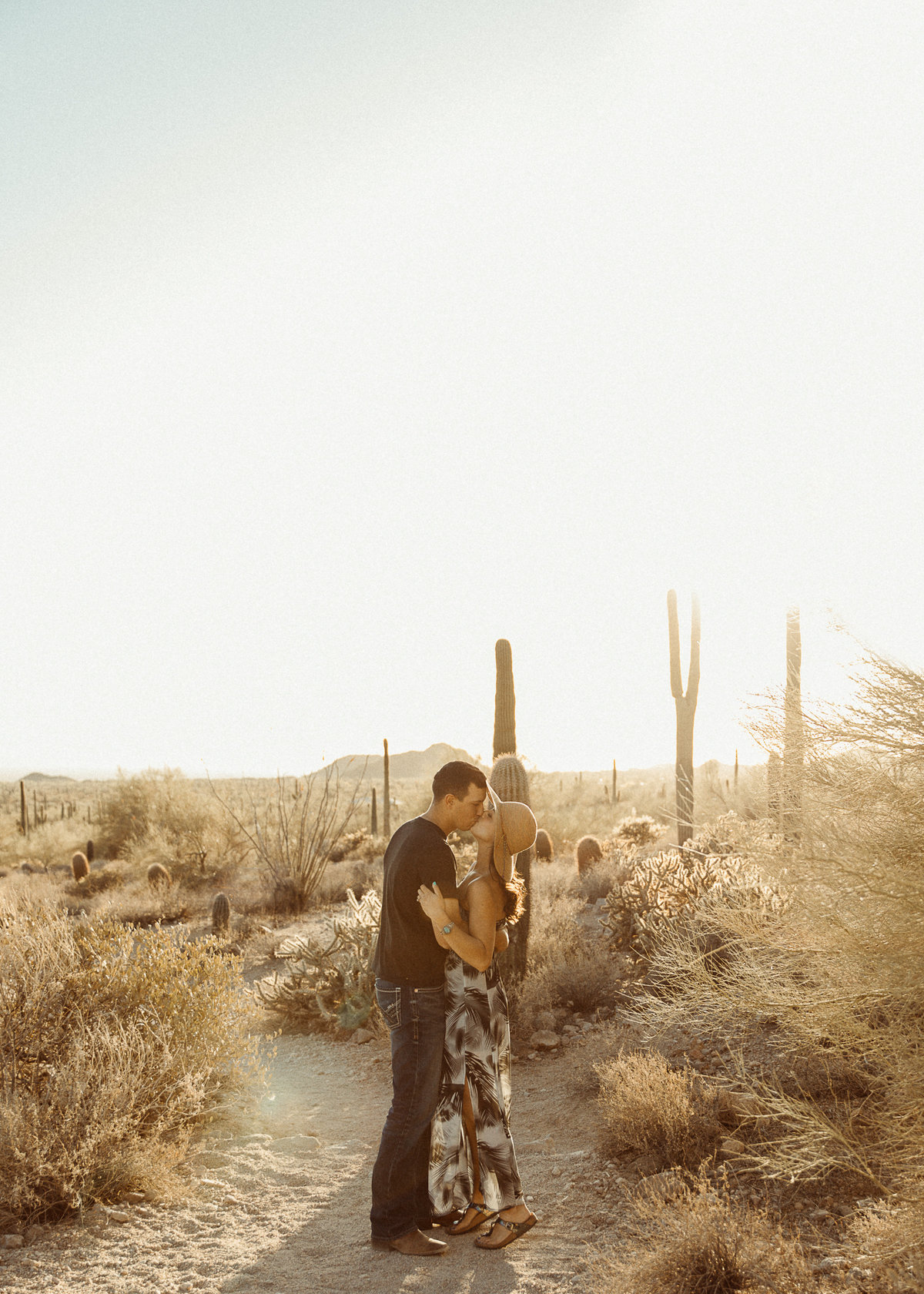 couple kisses in desert of Arizona with cacti and sun behind them
