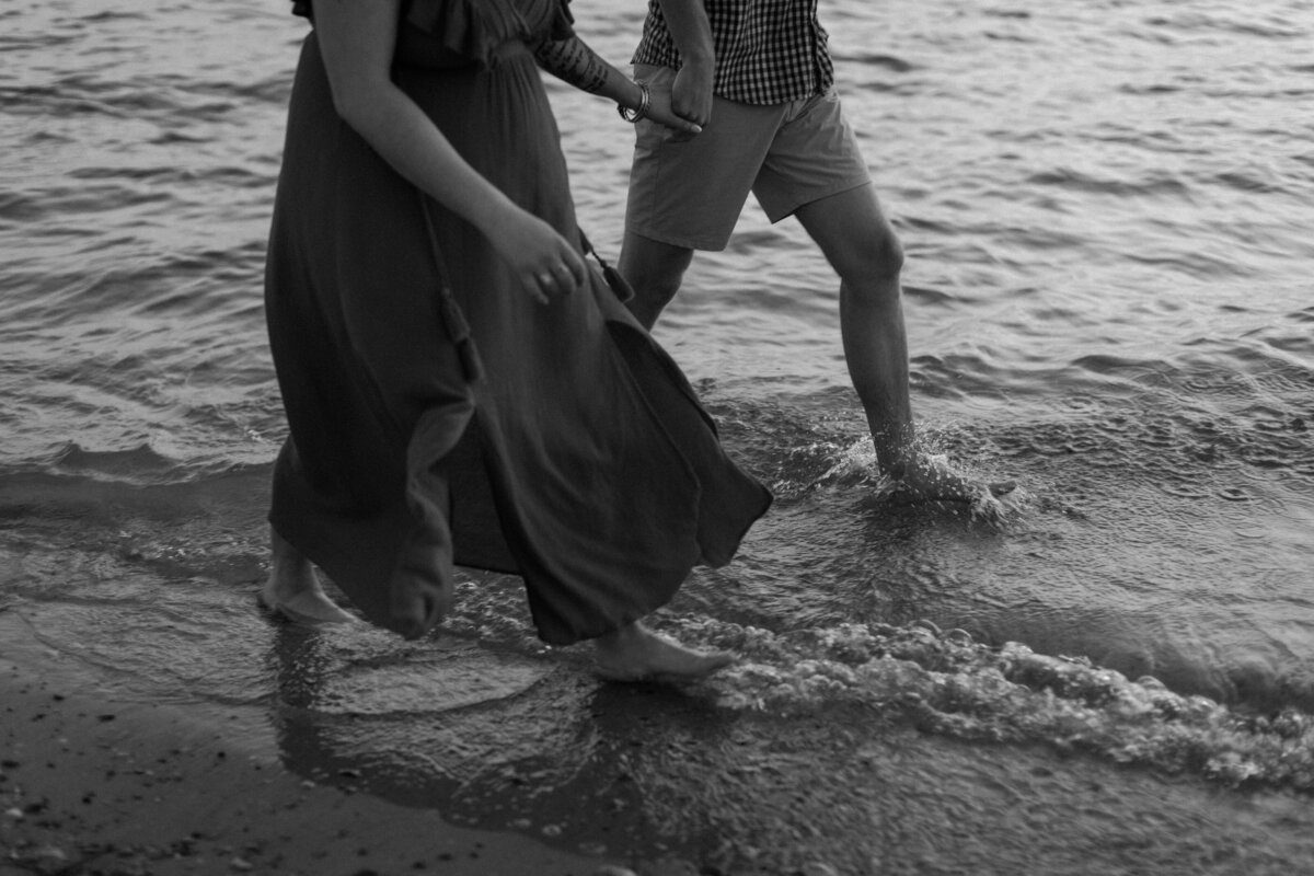 the legs and feet of a couple holding hands and walking in the water on the beach
