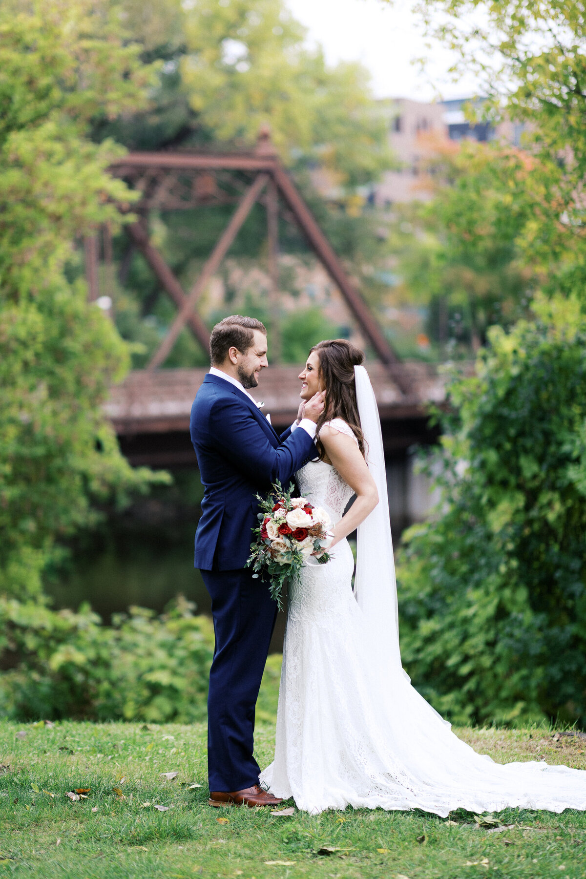 ​Bride and groom stand in Minneapolis, gazing at each other joyfully. The groom's hands gently touch the bride's face as she holds her wedding bouquet. Photograph captured by a Minneapolis wedding photographer.