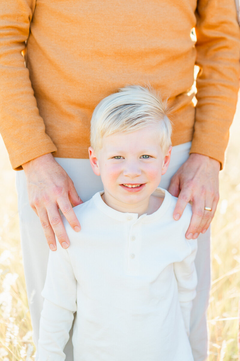 a young boy stands in front of his father and looks at the camera of his Austin, TX family photographer.