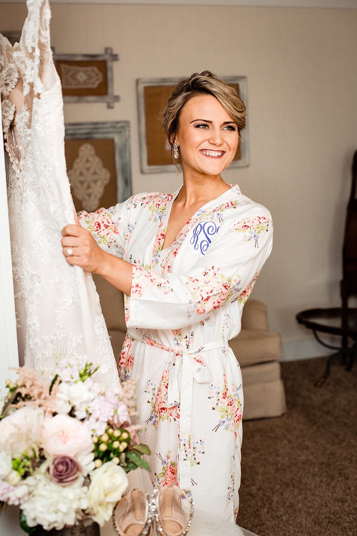 Bride is wearing a monogram white robe with flower pattern getting ready to take her dress off the hanger