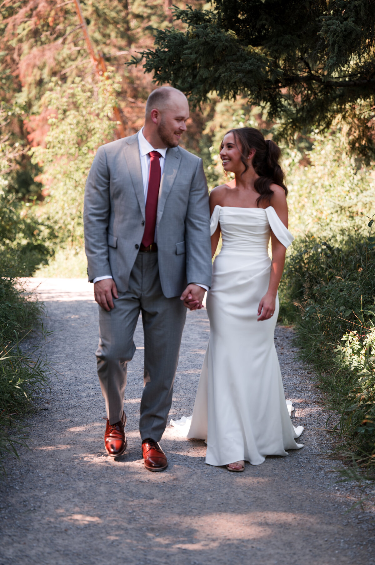 bride and groom walk hand in hand down a path in an Edmonton park