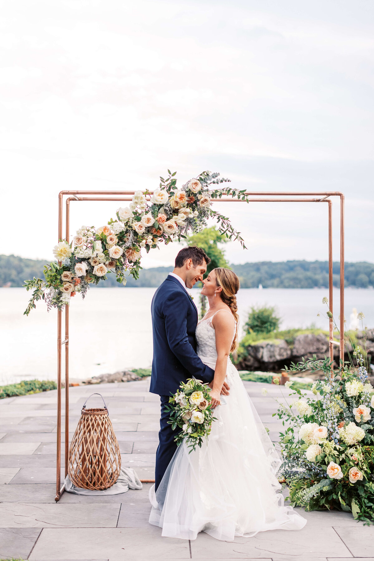 Bride and groom stand in front of their floral ceremony arch.