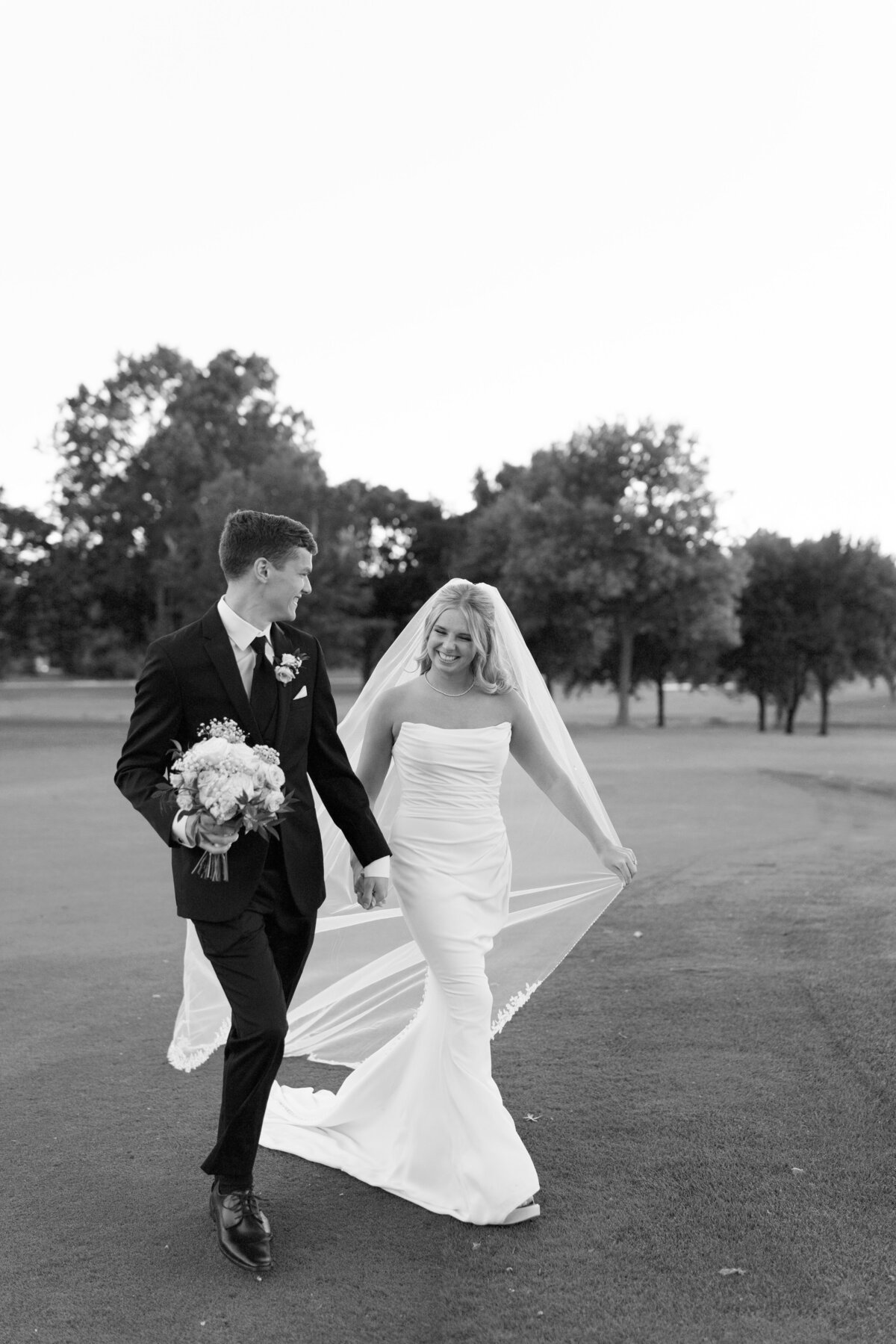 Groom holds bouquet and brides hand as they happily walk on the golf course where they were married taken by Illinois Wedding Photographer Lacey Graham 