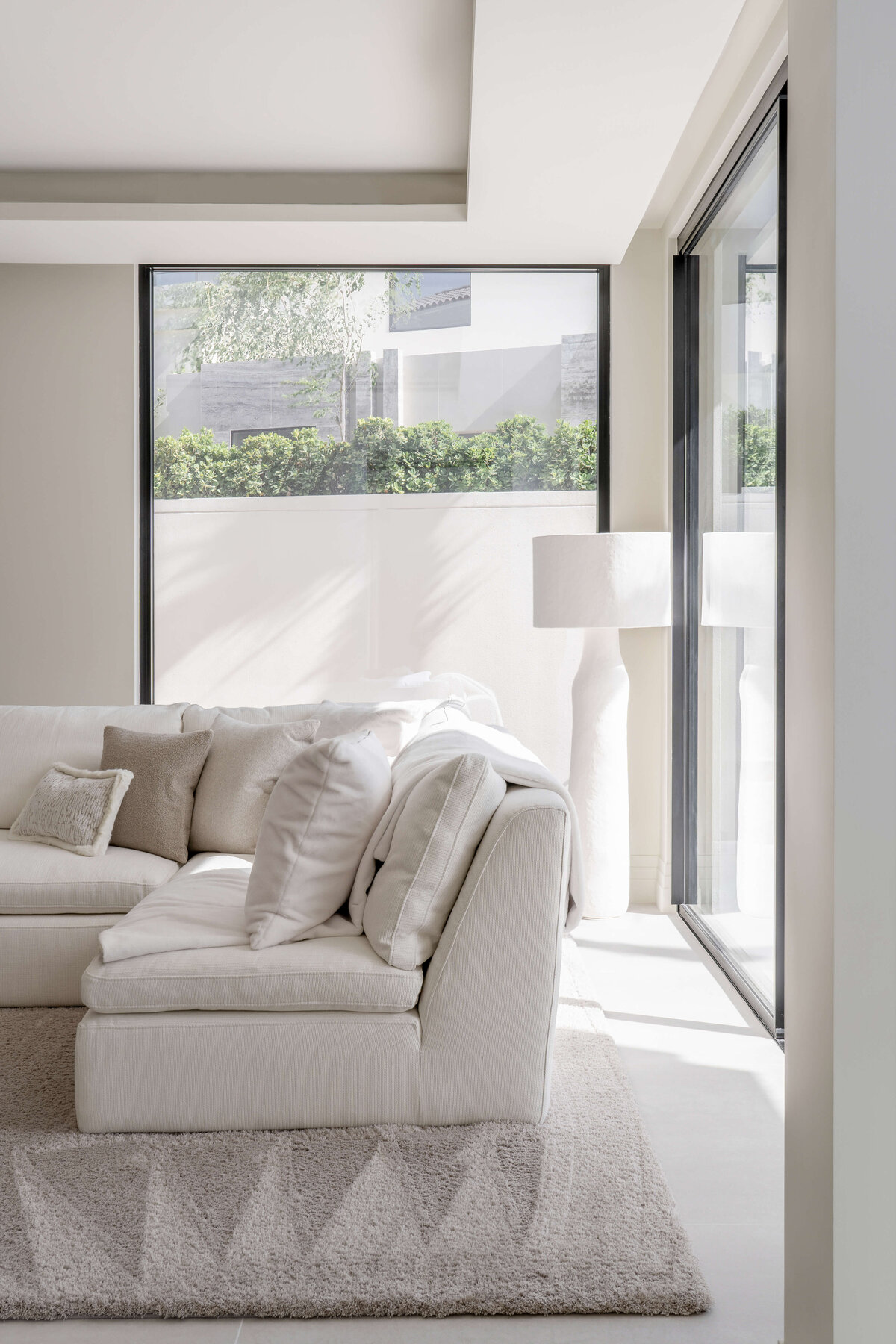 Large floor-to-ceiling windows in a bright, airy living room featuring a white couch atop a light, textured rug.