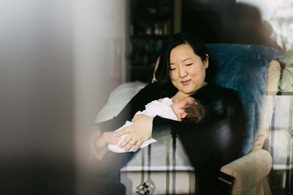 mother holding newborn son in a rocking chair from a  family session in her home.