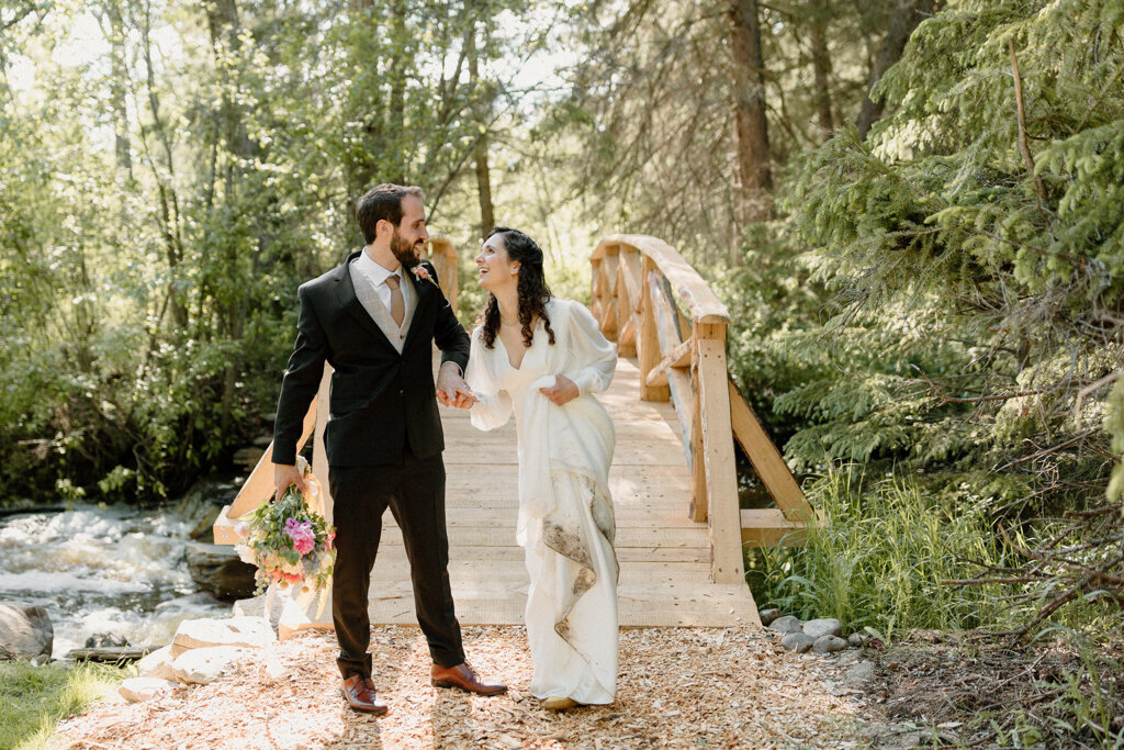 Elegant bride and groom at wooden bridge at The Valley Weddings, a rustic and majestic wedding venue in Westerose, Alberta, featured on the Brontë Bride Vendor Guide.