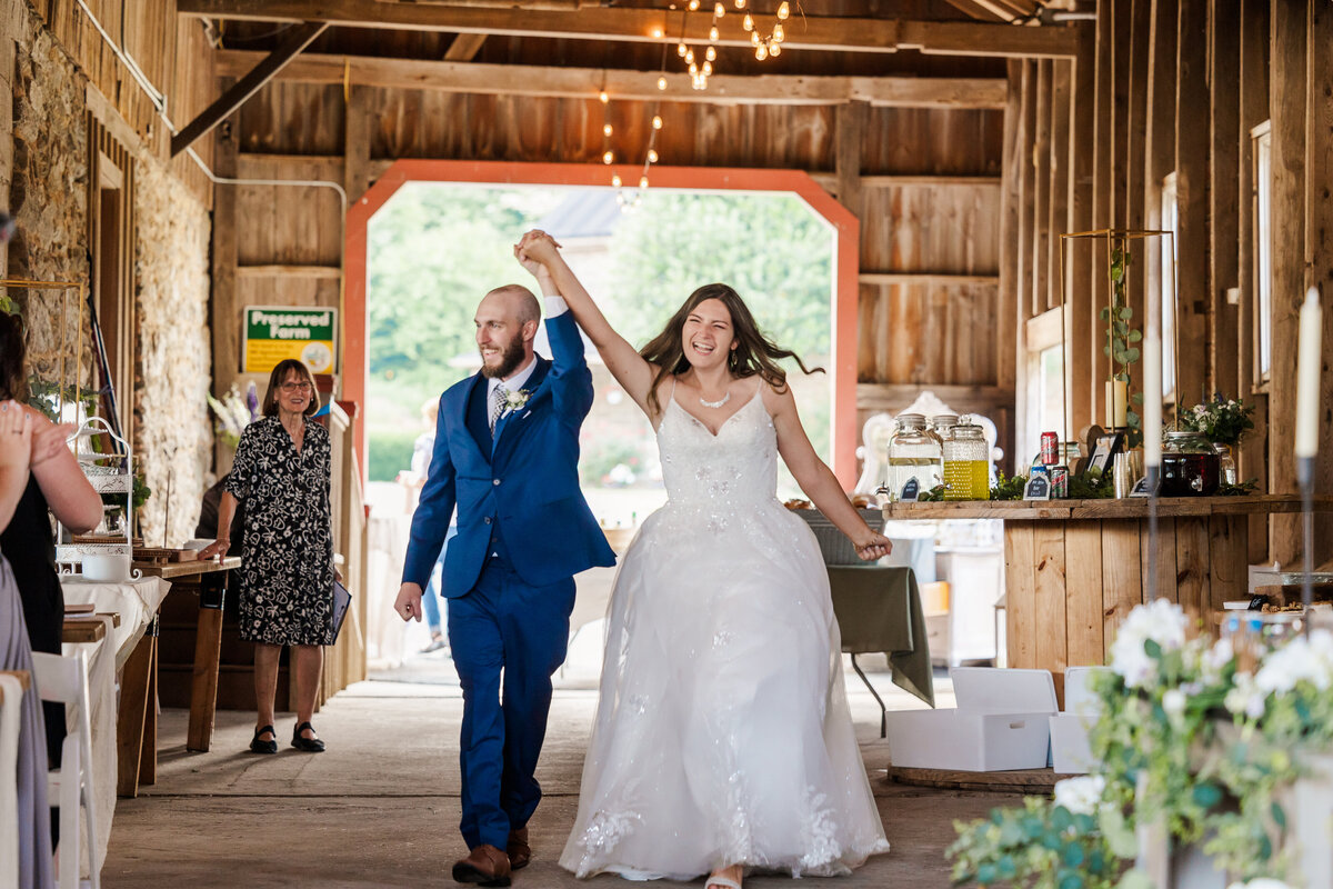 wedding couple smiling and holding hands in barn walking into reception