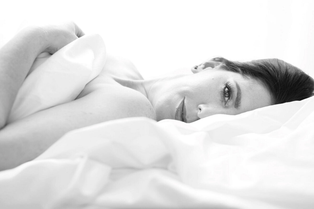 Woman laying in white sheets with only half of her face showing