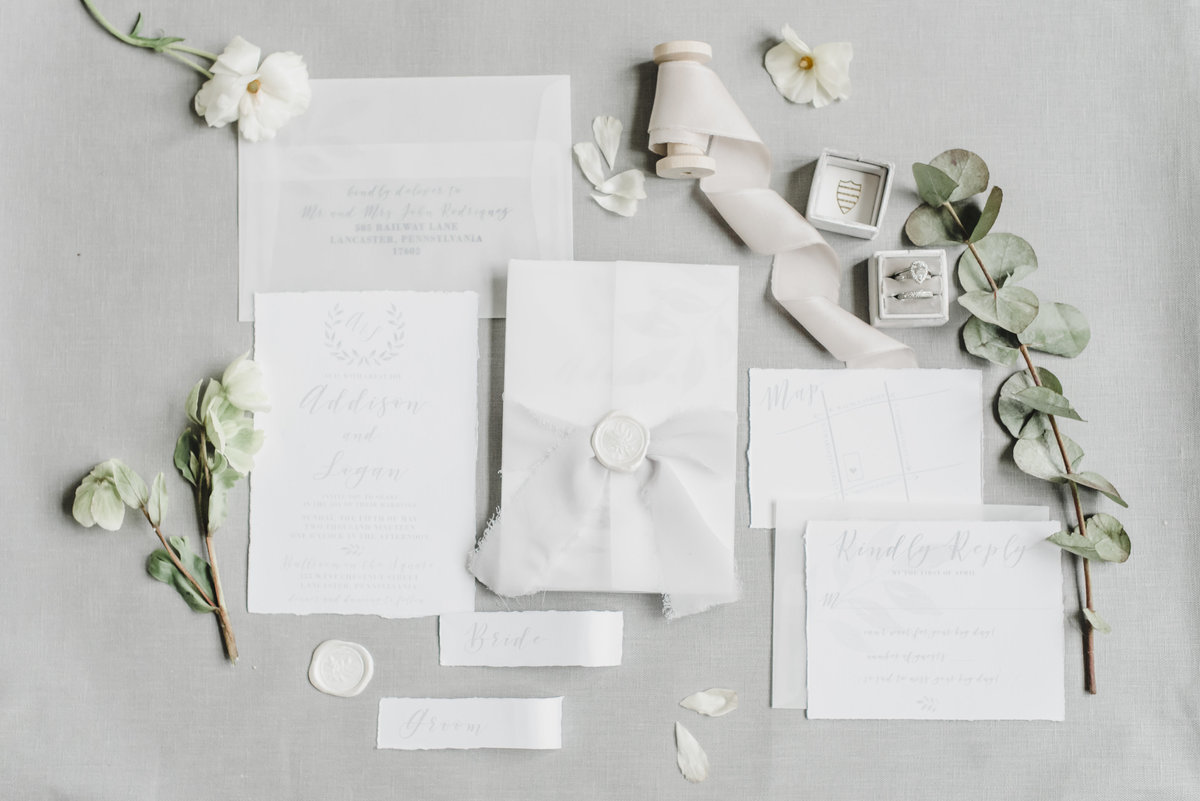 ivory stationery suite laying on a light grey backdrop surrounded by small greenery