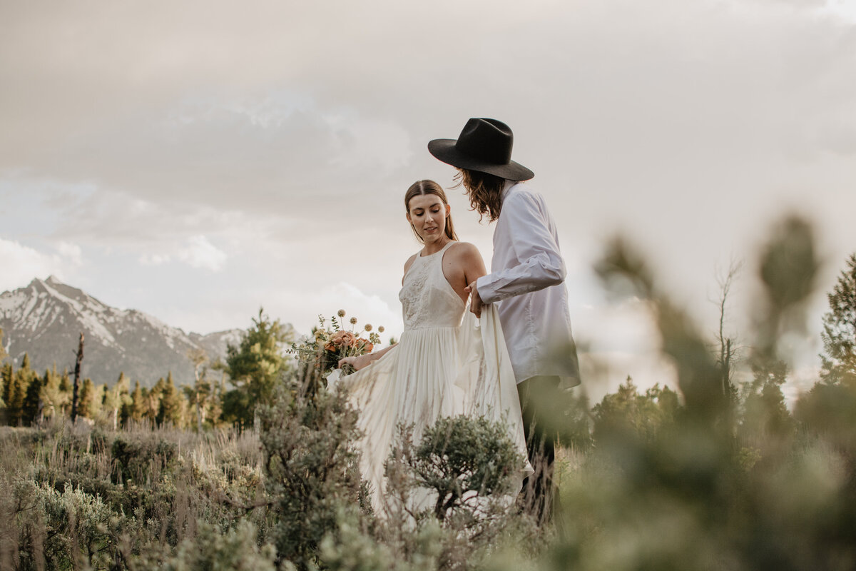 wyoming elopement with bohemian styled couple walking through a meadow with the mountains in the distance as they talk together for candid wedding pictures