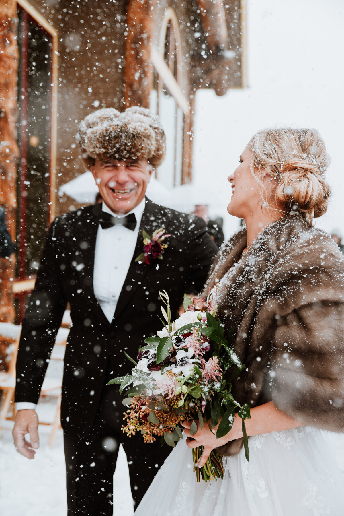 Bride and father laugh under falling snow at cozy winter wedding at the Lodge at Breckenridge.