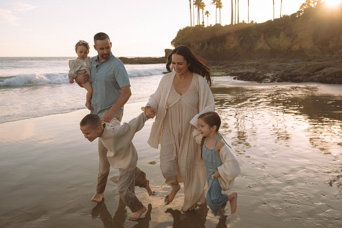 Family running along the shoreline during sunset at Laguna Beach, captured by Orange County photographer Maria Alcantara.