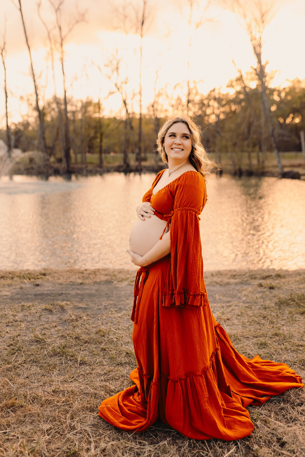 Livingston TX maternity photo—pregnant woman by water in flowing orange gown.