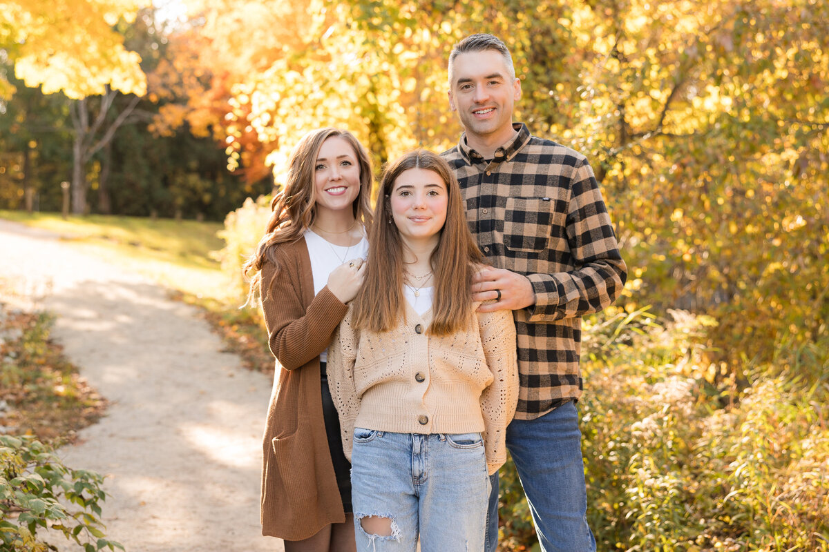 A family is standing together with beautiful fall leaves behind them and smiling at the camera