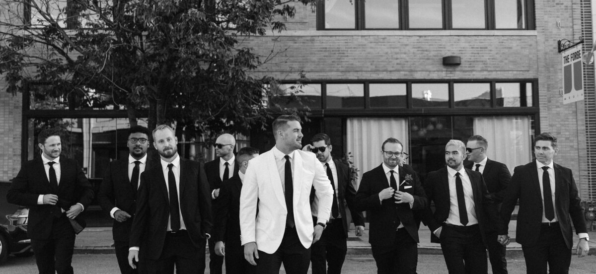 Black and white photo of a group of men in suits walking confidently on a city street