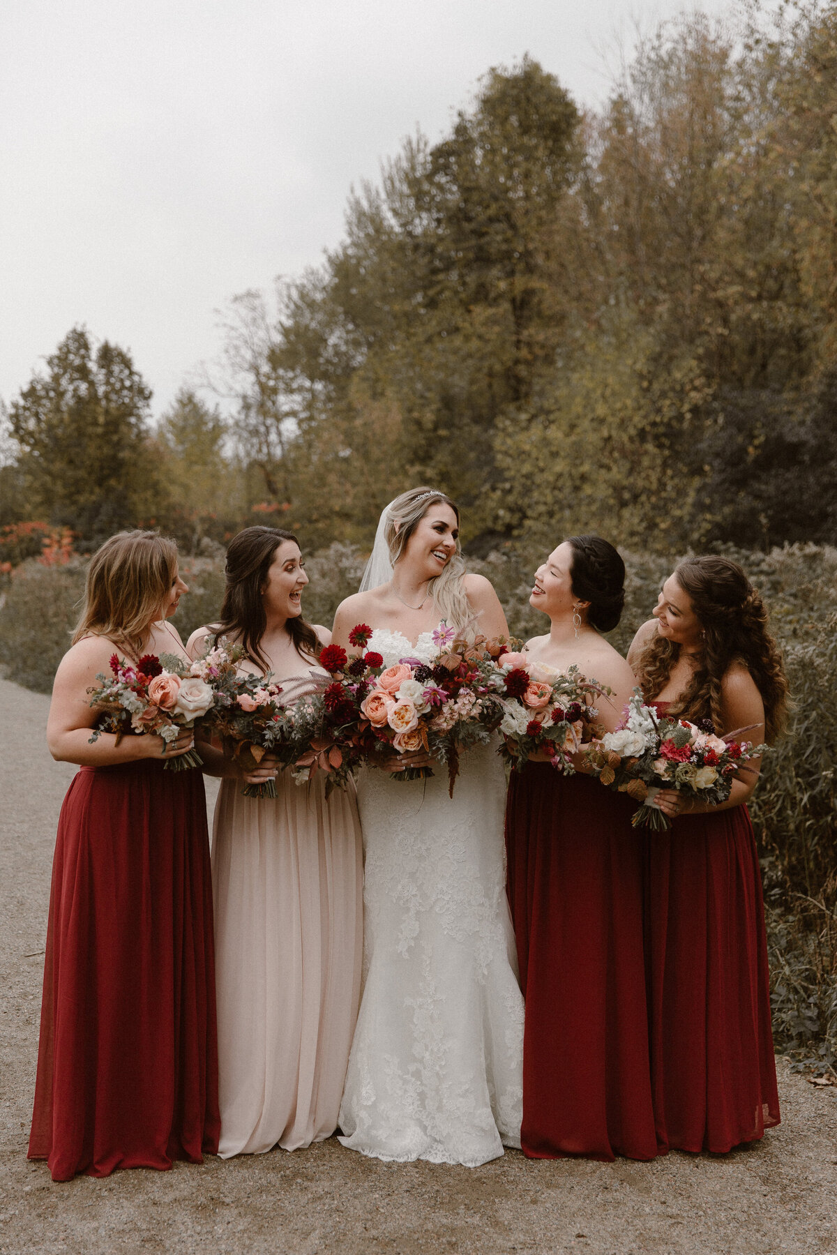 Bridal party in a tree lined park in Montreal, holding red flower bouquets.