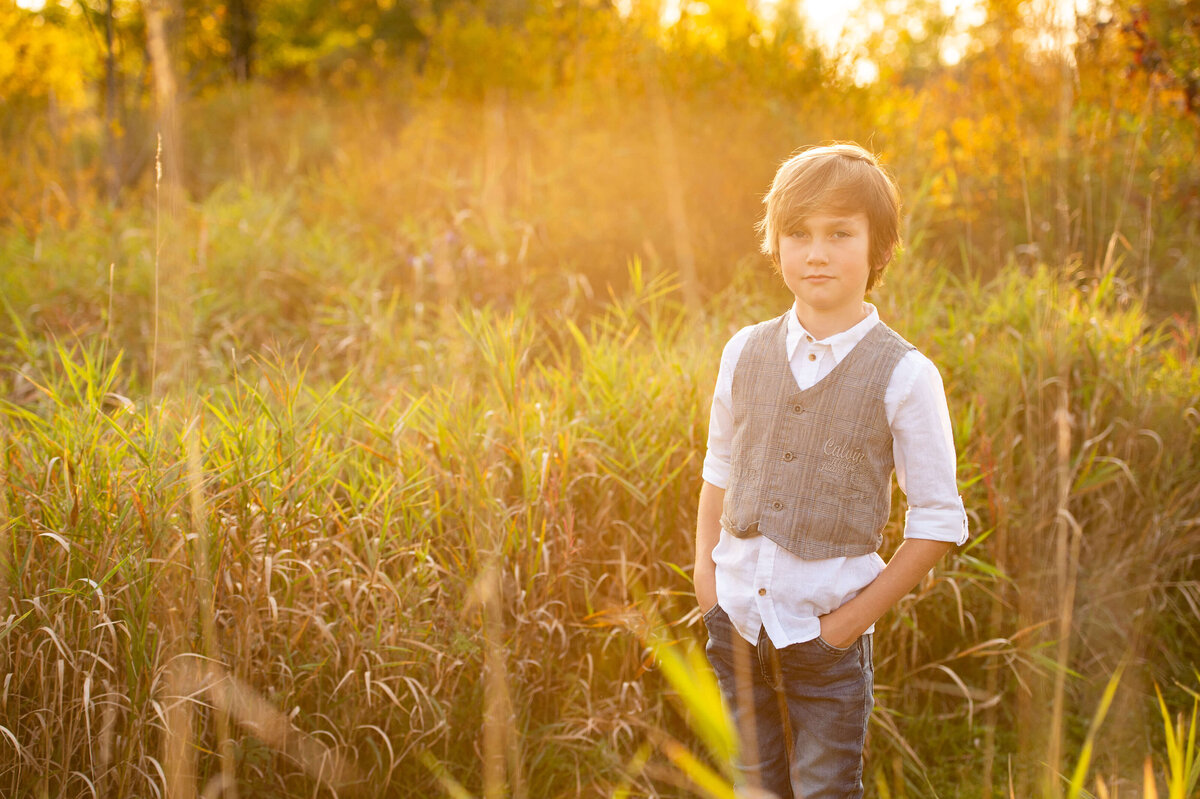 a young boy standing in a field at golden hour as part of a family photography session in Ottawa