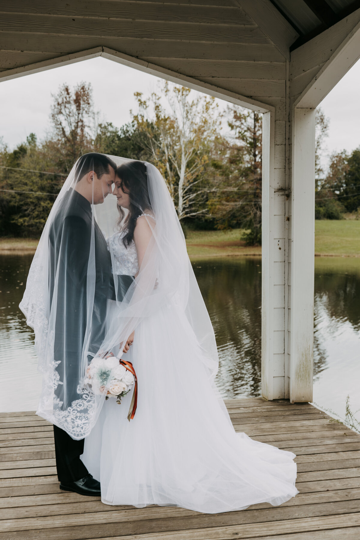 Amber and Josh at Kincaid Manor, standing under a gazebo by a pond, foreheads touching, draped in her veil.