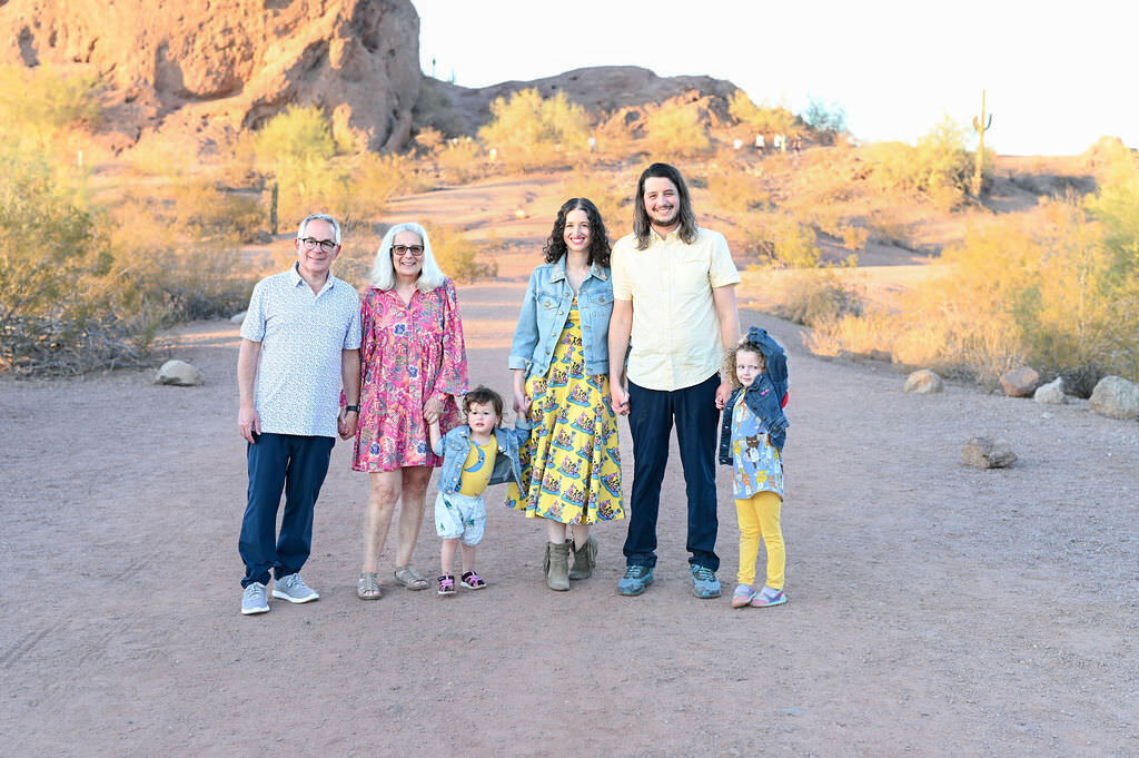 An extended family smiling while standing in a graveled area next to a rock formation.