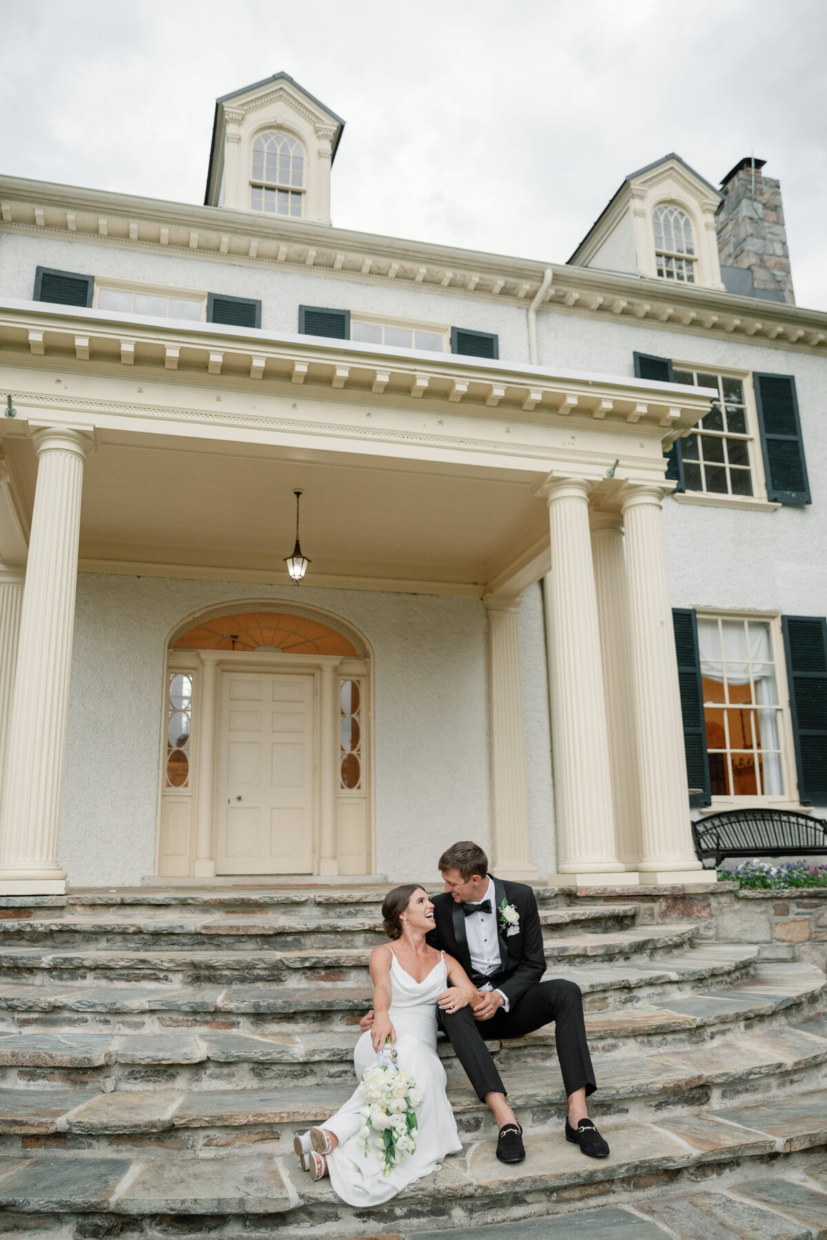 Bride and Groom sit on the steps of Rust Manor House