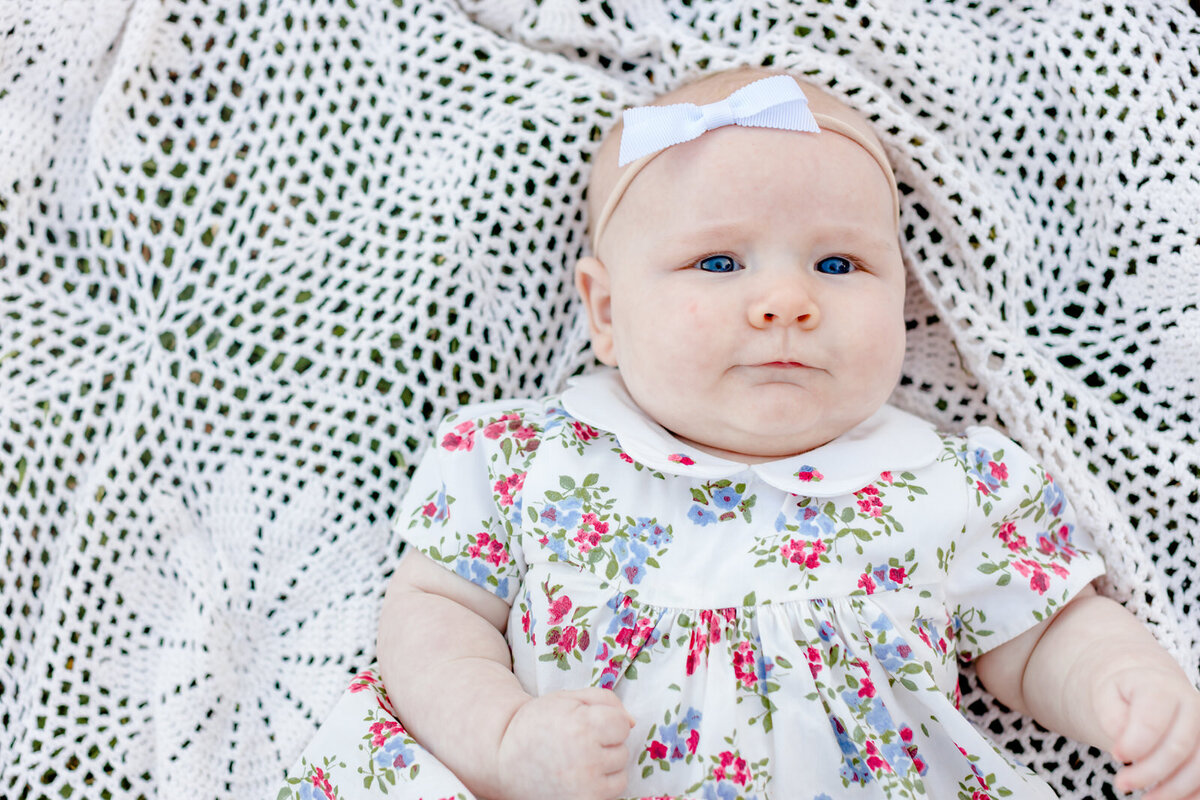 Infant girl lays on white blanket and smiles during family session at Little Mulberry Park