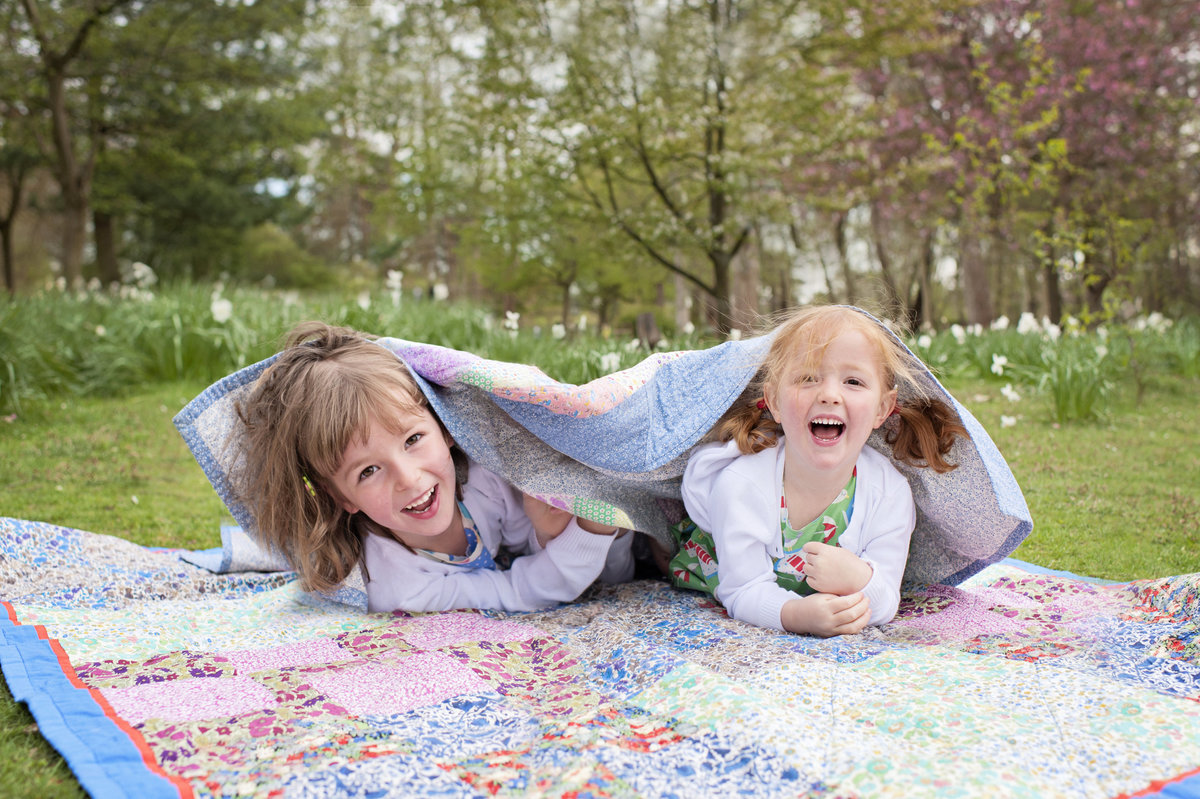 Two sisters play peek-a-boo under a blanket in Bushy Park, Teddington