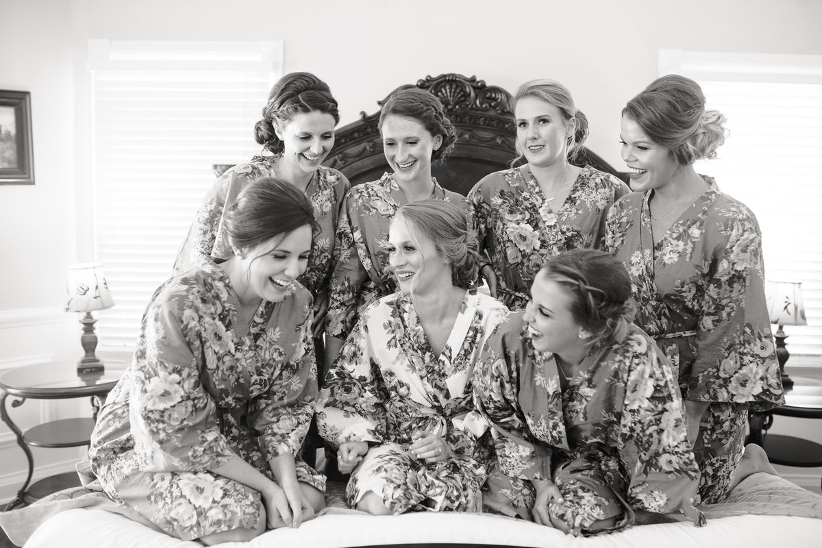 Bride and bridesmaids, wearing matching robes, laugh together before the ceremony.