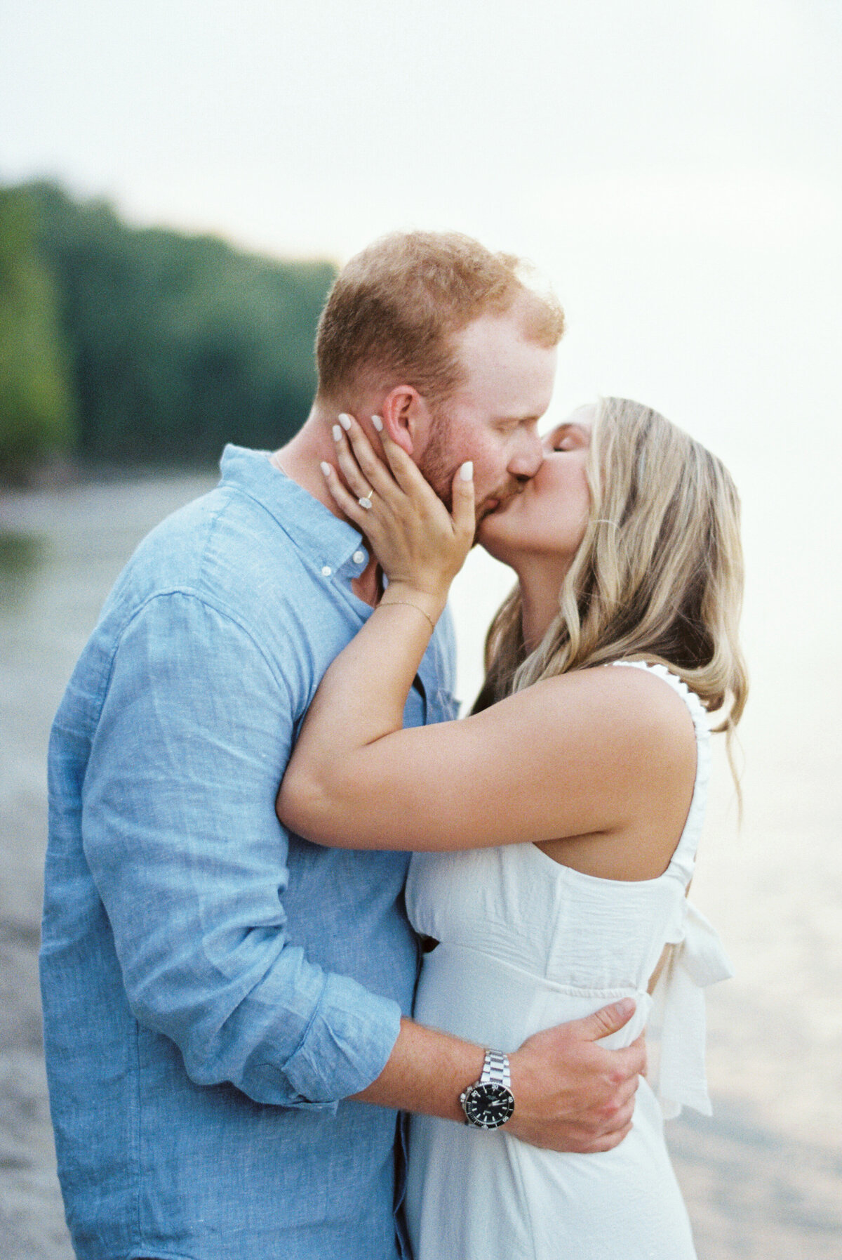 Close-up of couple kissing at Edgewater Beach, bride showing engagement ring.

