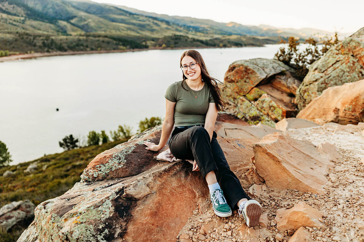 High school senior girl sitting on the rock cliff at Horsetooth Reservoir.