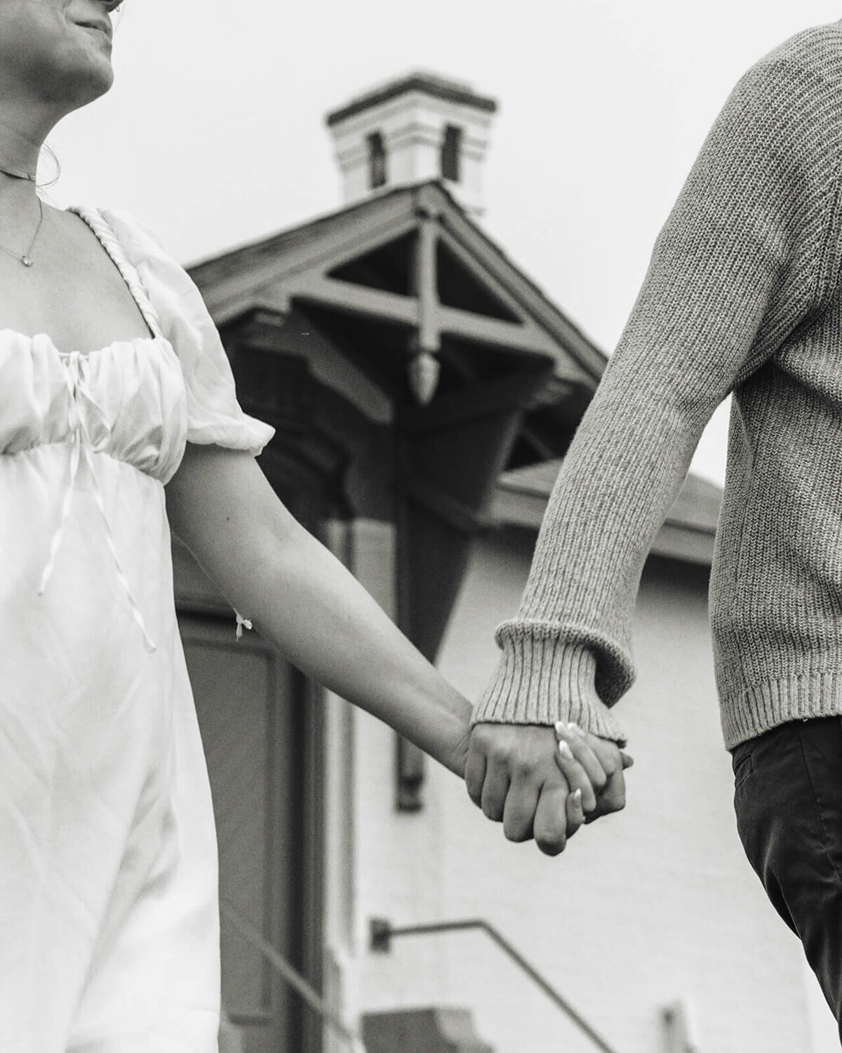 Black and white image of faceless couple holding hands with a lighthouse in the background. 