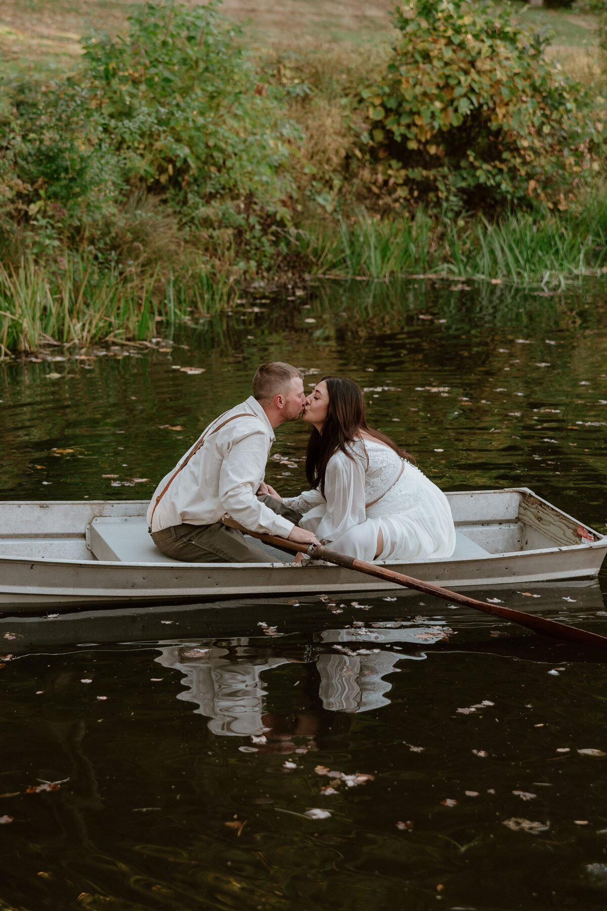 Romantic engagement photo of a couple kissing in a rowboat on a pond in Southbury, Connecticut, surrounded by fall greenery.